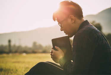 image of a husband praying with the Christian bible, sitting in a field