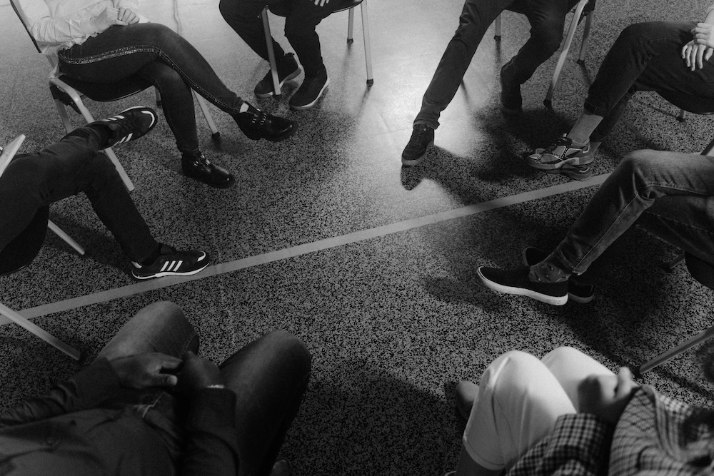 A warm, kind group of people sitting in a circle, engaged in a porn addiction recovery support group, demonstrating peer support and shared healing.