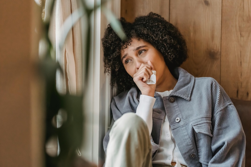 A woman sitting on the floor leaning against a wall in a moment of reflection, representing the emotional shock and crisis of betrayal trauma.