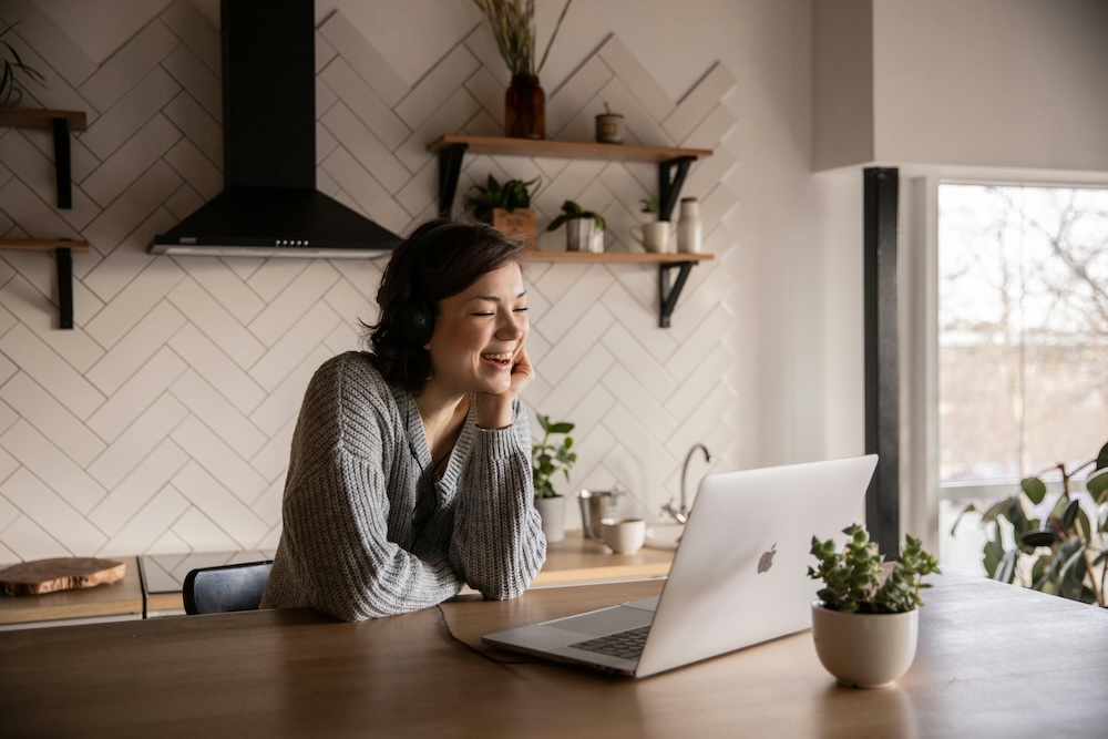 A relaxed and happy woman in her kitchen on a video call, demonstrating the convenience and safety of accessing specialized online counselling for trauma.
