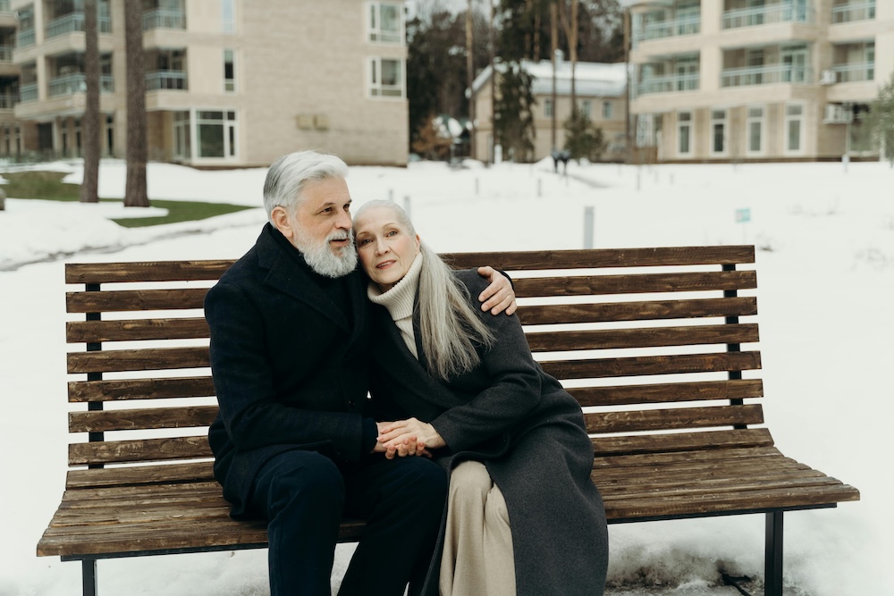 An older couple sitting close on a park bench holding hands, symbolizing the ability to heal attachment injuries and build secure emotional intimacy after trauma.