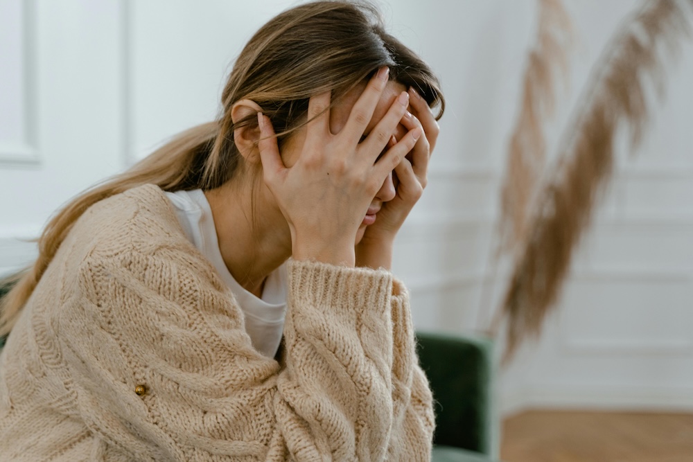 A woman rubbing her temples to show the stress and brain fog caused by the neurobiological impact of betrayal trauma on the body.
