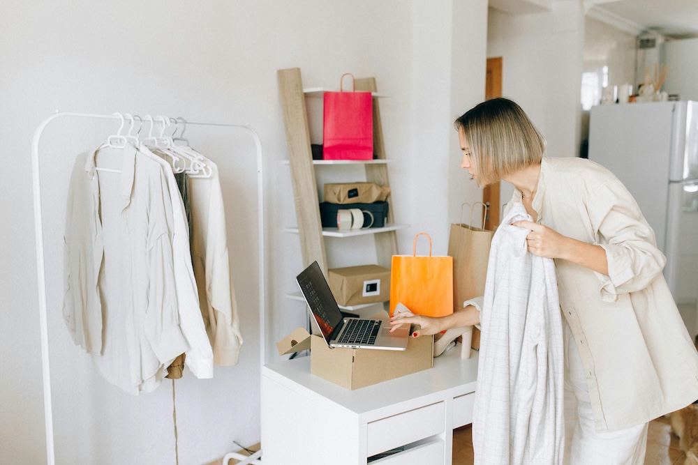 A woman multitasking between working on a laptop and cleaning her room, depicting compulsive busyness and the inability to rest often found in high-functioning trauma survivors.