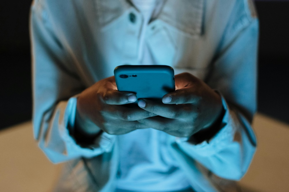 Person holding a glowing smartphone in a dimly lit room, highlighting the digital aspect of scanning behaviors in recovery.