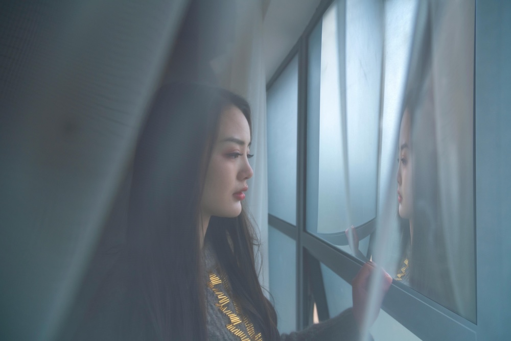 A woman looking thoughtfully out a window into a foggy morning, representing the confusion and isolation caused by gaslighting.