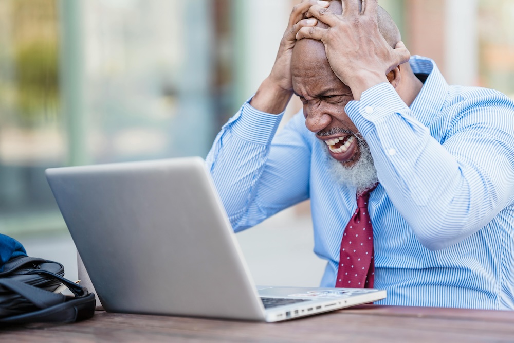 A man leaning over his desk with his head in his hands, portraying the emotional exhaustion and stress that serve as triggers for maladaptive coping mechanisms.