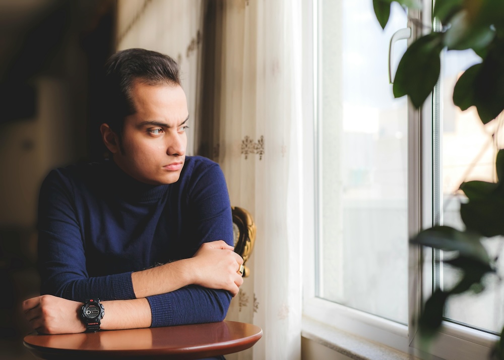 A man gazing out a window in a contemplative state, symbolizing the deep self-reflection required to address the root causes of addiction.