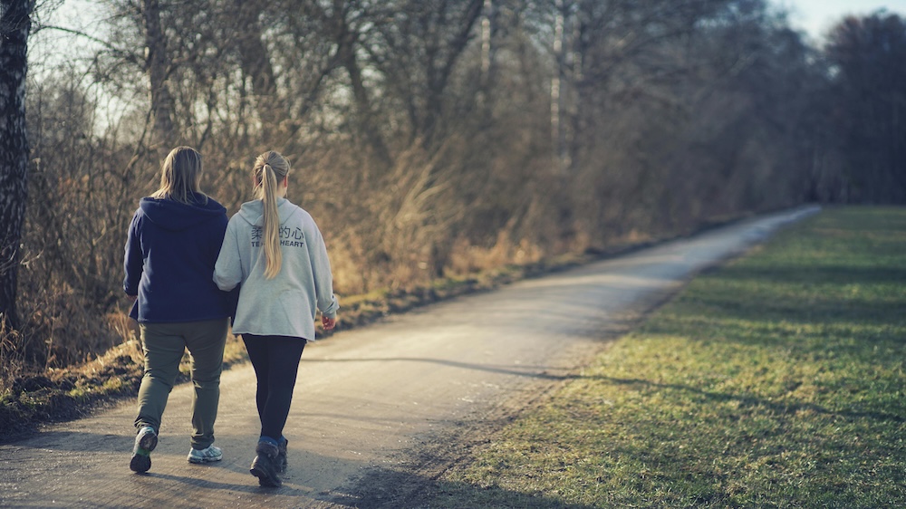 Two people walking side-by-side through a green park, symbolizing the professional support and companionship found in trauma recovery.