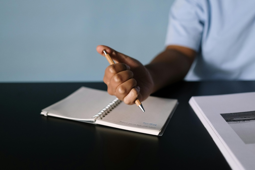 A person's hand writing a structured list in a notebook, representing the organized and therapeutic process of preparing a formal disclosure.