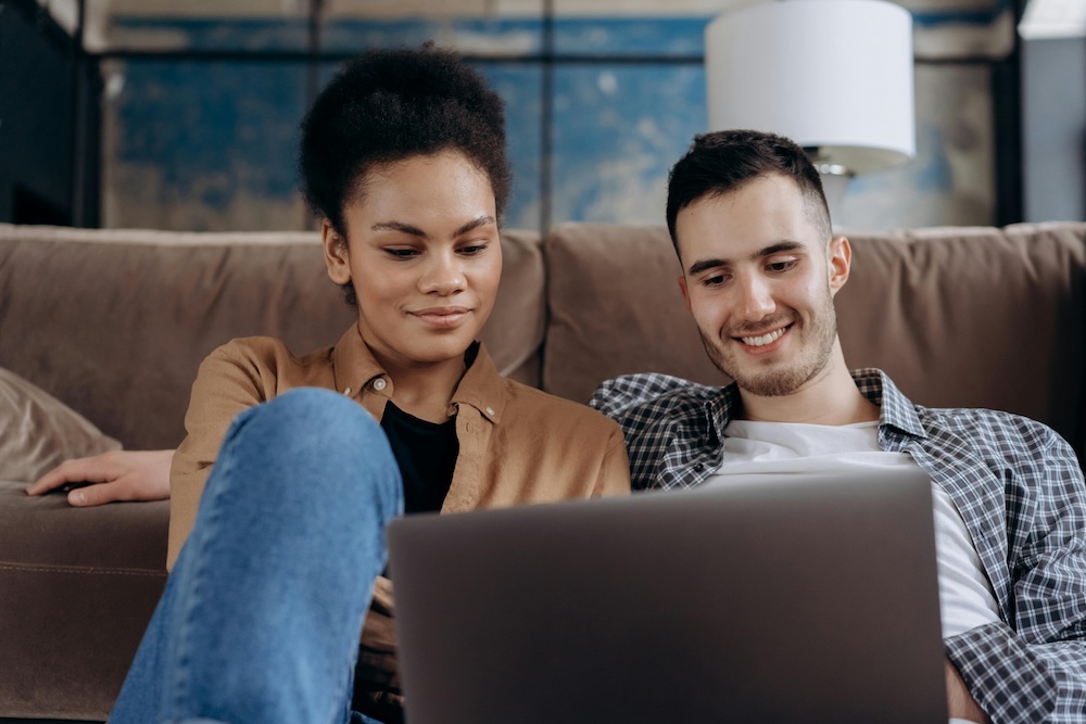 A couple sitting together looking at a laptop screen during an online therapy session, taking steps to break their negative interaction cycle.