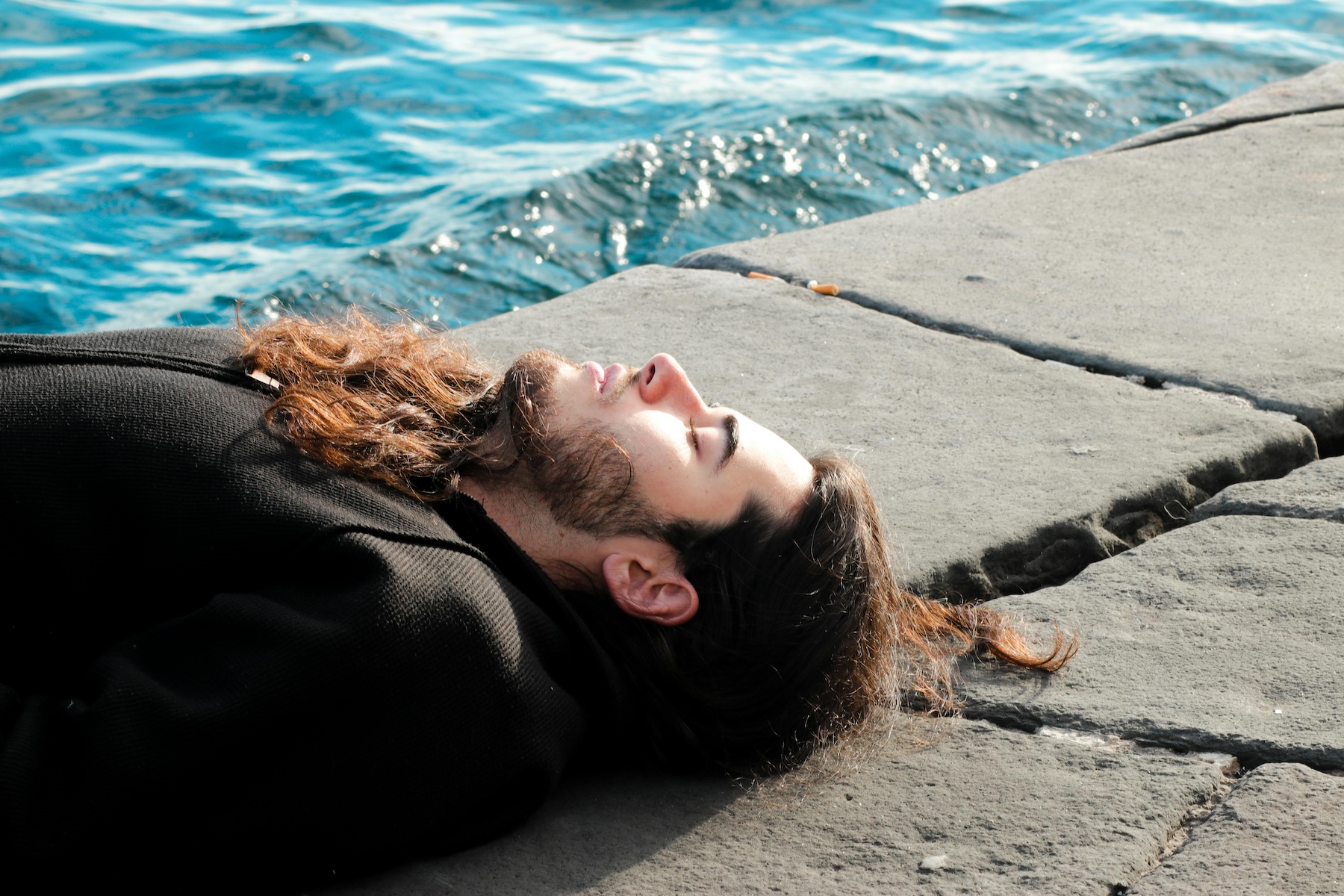 A person lying in a peaceful outdoor setting, eyes closed, taking a deep breath to represent emotional grounding and self-care.