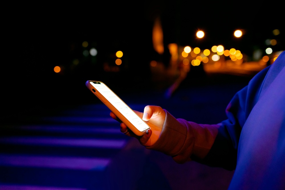 A close-up of a hand holding a smartphone in a dimly lit room, symbolizing the secretive nature of digital compulsion.