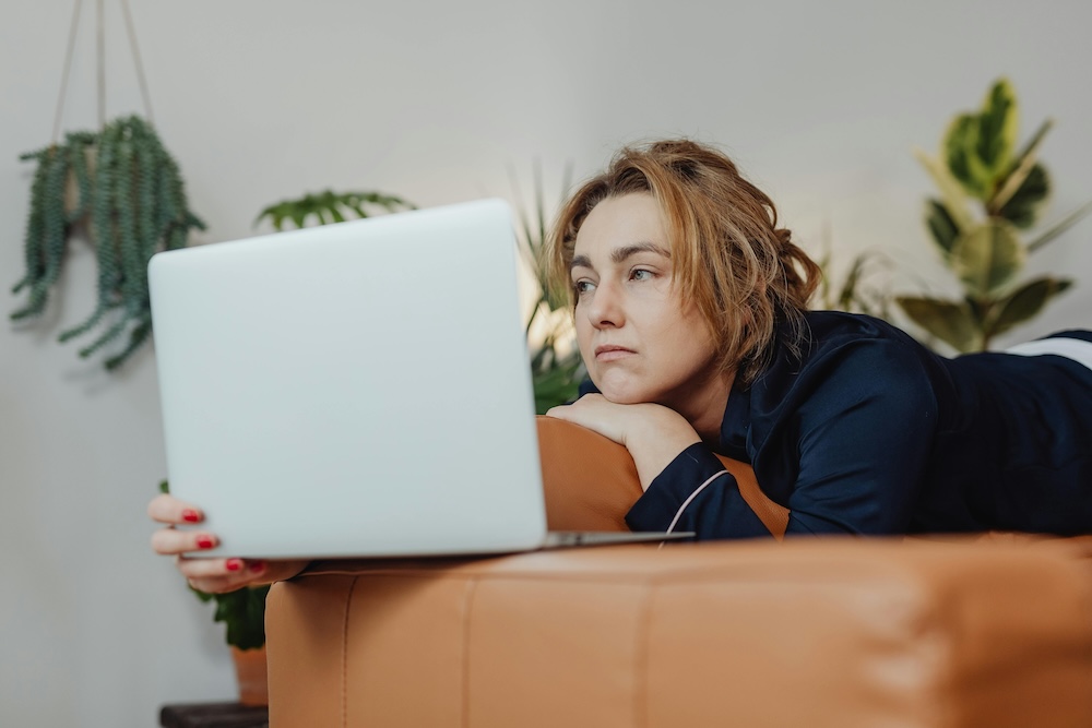 A woman in a home office looking at her laptop with a hopeful expression, ready to book an online therapy session.