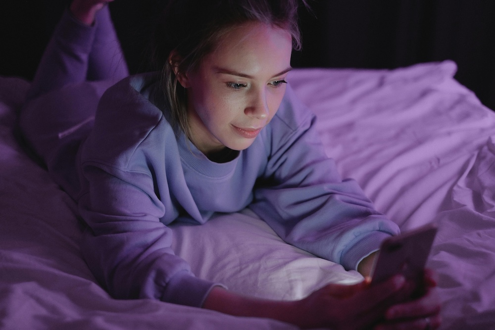 female pornography use — woman alone on couch looking at phone at night