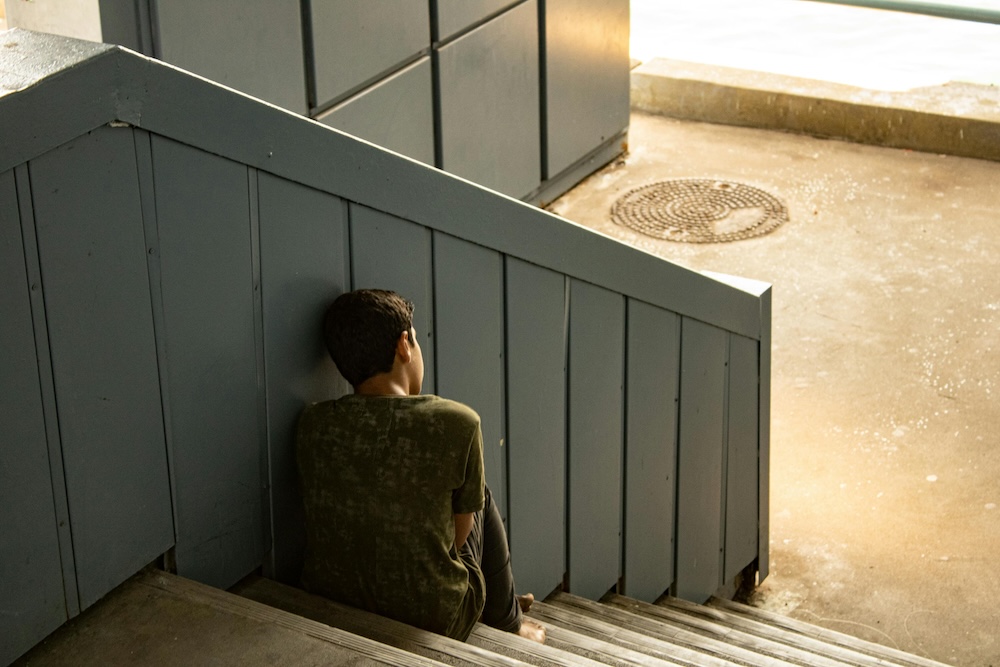 betrayer shame recovery. A person sitting alone in a quiet stairway, head lowered, the moment when shame floods in