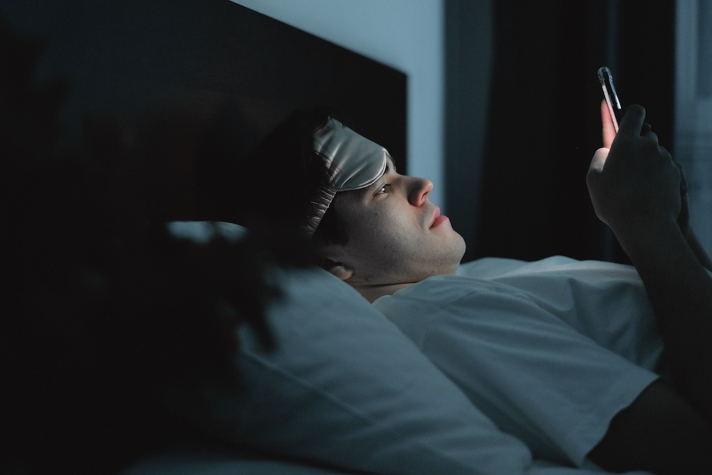 Porn induced erectile dysfunction conditioning — a man's face lit by a phone screen in a dark room.