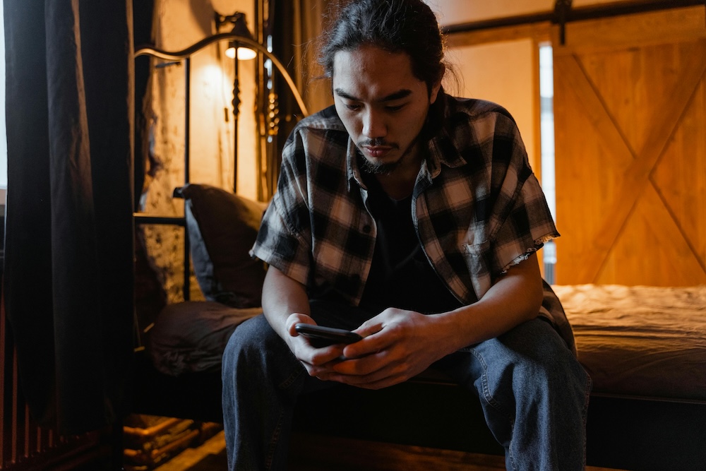 compulsive porn use despite wanting to stop -- person sitting on edge of bed late at night, phone face down, looking exhausted