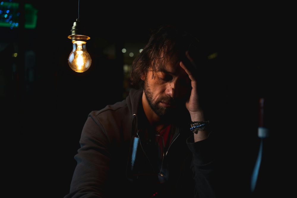 person sitting alone in dim light, contemplative, hand to face, vocabulary ahead of empathy in early recovery