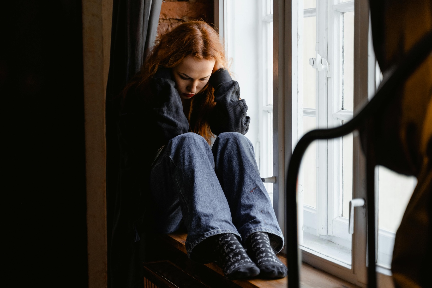 Why does the betrayer keep hurting their partner. A person sitting alone by a window in soft natural light, looking inward