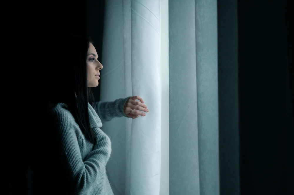 betrayed partner -- a woman alone by a window in soft light, holding a difficult moment