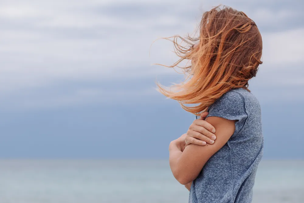 The crash after hysterical bonding: person sitting quietly alone by a window in soft light, feeling grief surface