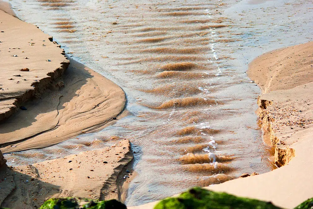 Water carving deepening channels through beach sand, the way repeated use redraws an arousal template