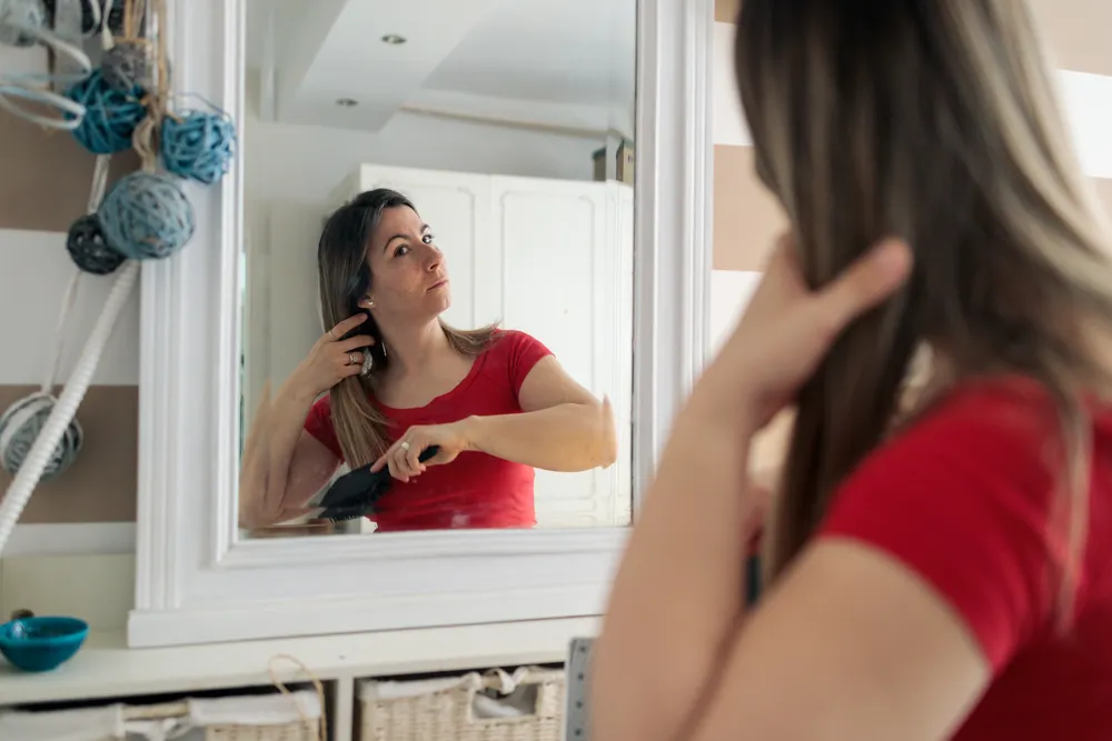 Woman studying her reflection in a home mirror, the body image wound of betrayal trauma