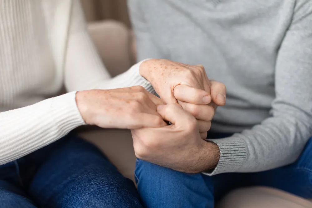 Two hands held steady in warm light offering the co-regulation that helps a betrayed partner feel safe