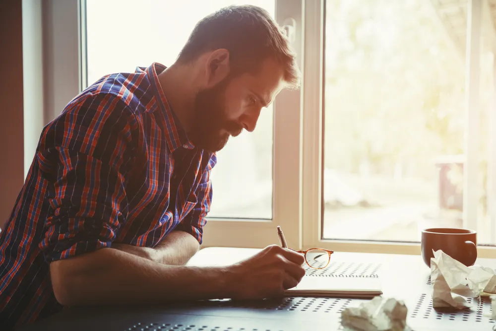 Man journaling at a desk by a window in morning light, reflecting on what an urge was medicating
