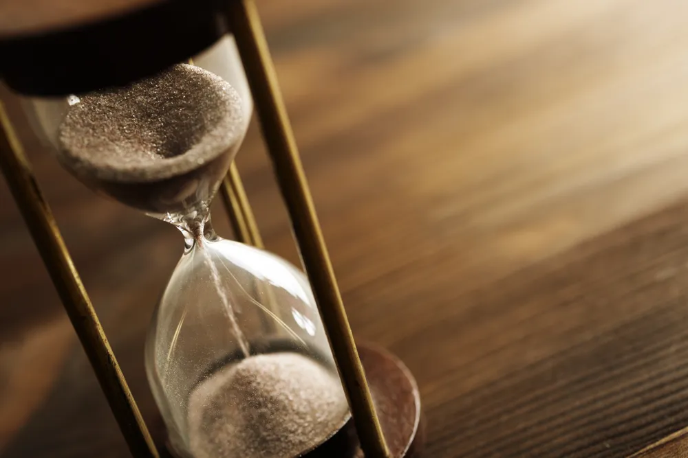 Sand falling through an hourglass on a wooden table, the evidence gathering slowly over time