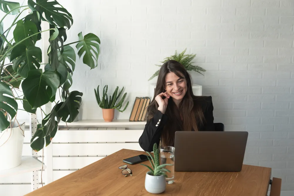 A person smiles during an online therapy session at a laptop, practicing connection from home.