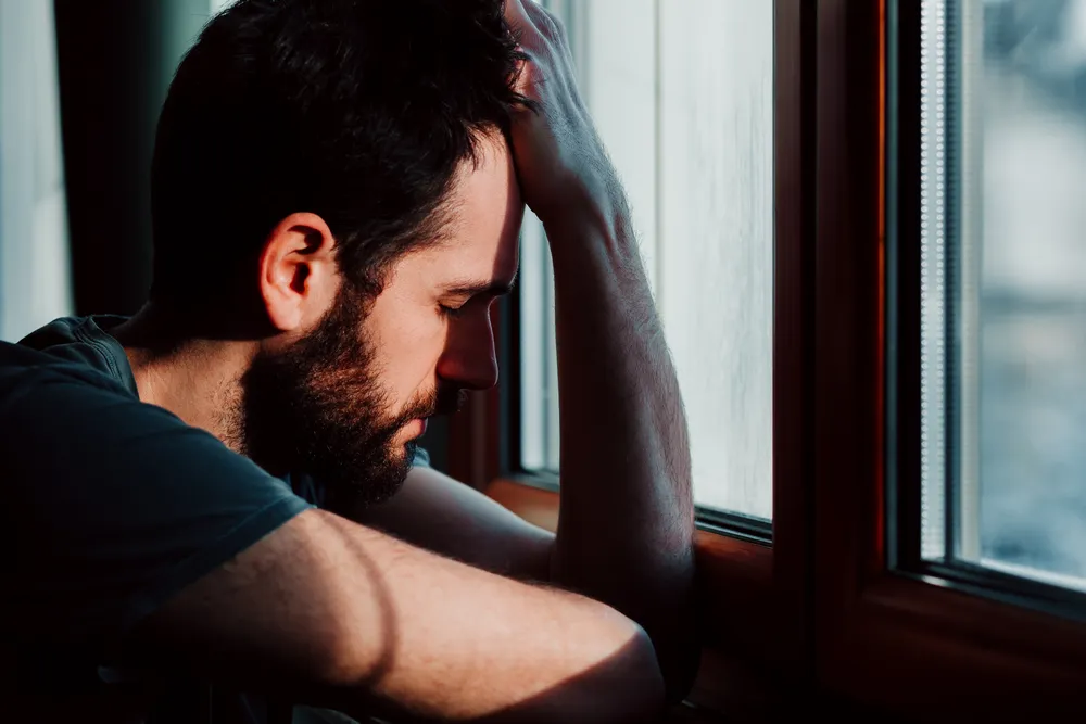 Man sitting by a window with his head resting on his hand, carrying a heavy weight