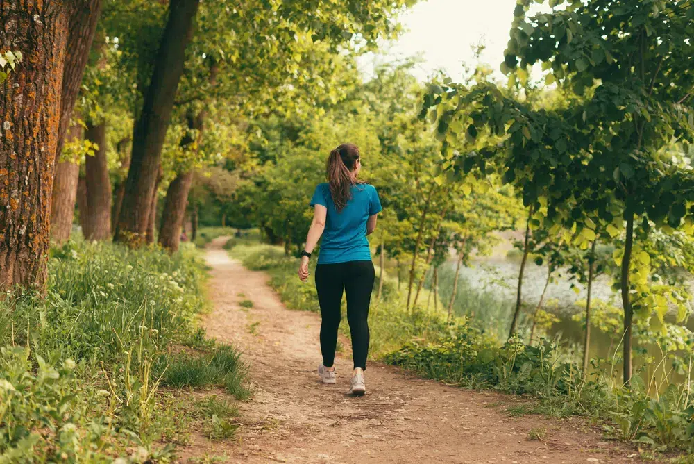 Woman walking a quiet tree-lined path, practicing urge surfing by moving toward a better reward