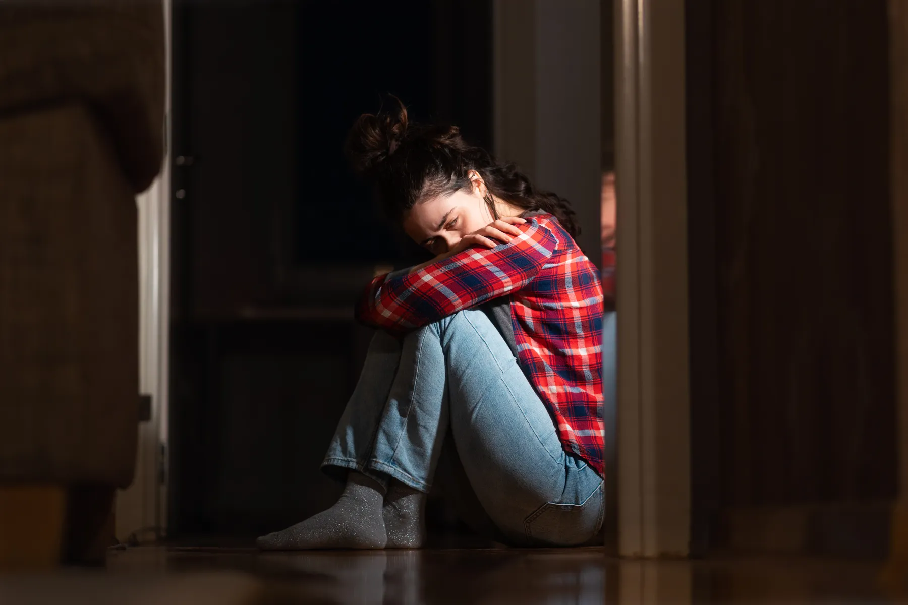 A person sitting on the floor against a wall, alert and unsettled, illustrating that betrayal trauma symptoms are real