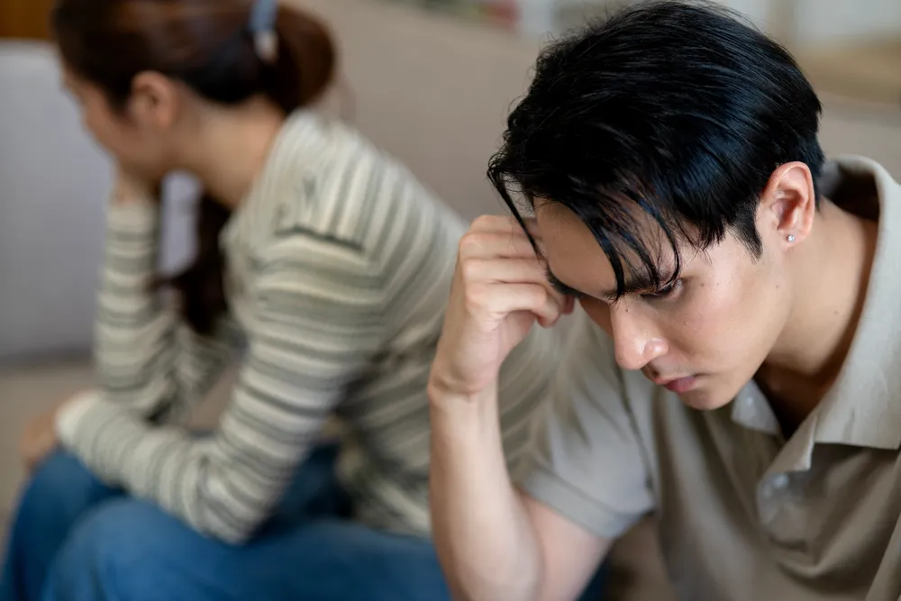 Two people sitting apart in a room, one turned away, an image of emotional withdrawal during a hard conversation