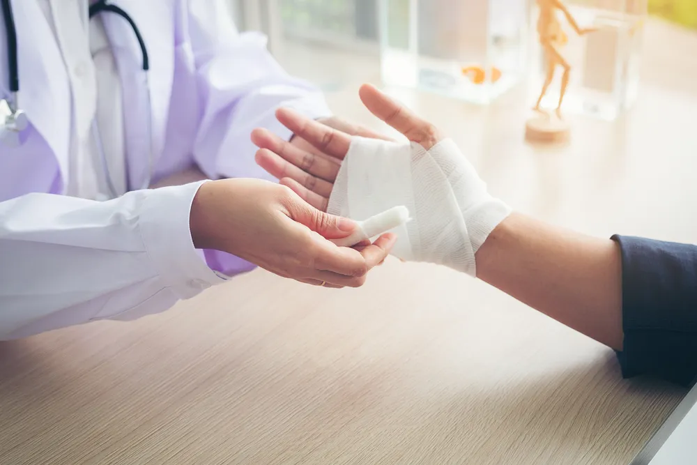 A clinician wrapping a bandage around an injured hand, the slow tending that follows the injury