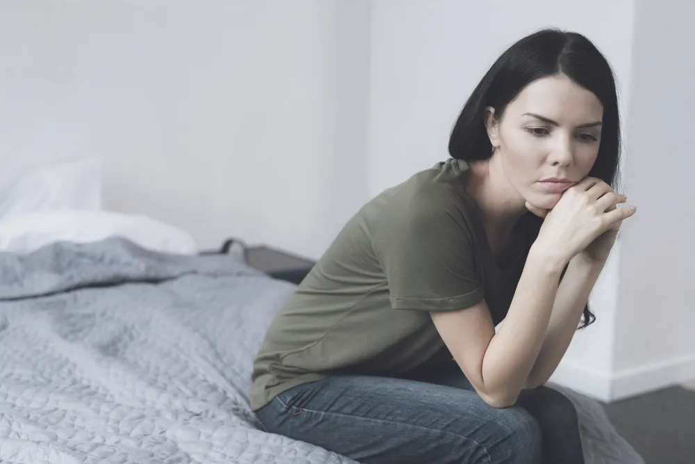 Woman sitting on the edge of her bed with her chin on her hands, carrying the shame that keeps compulsive lying going