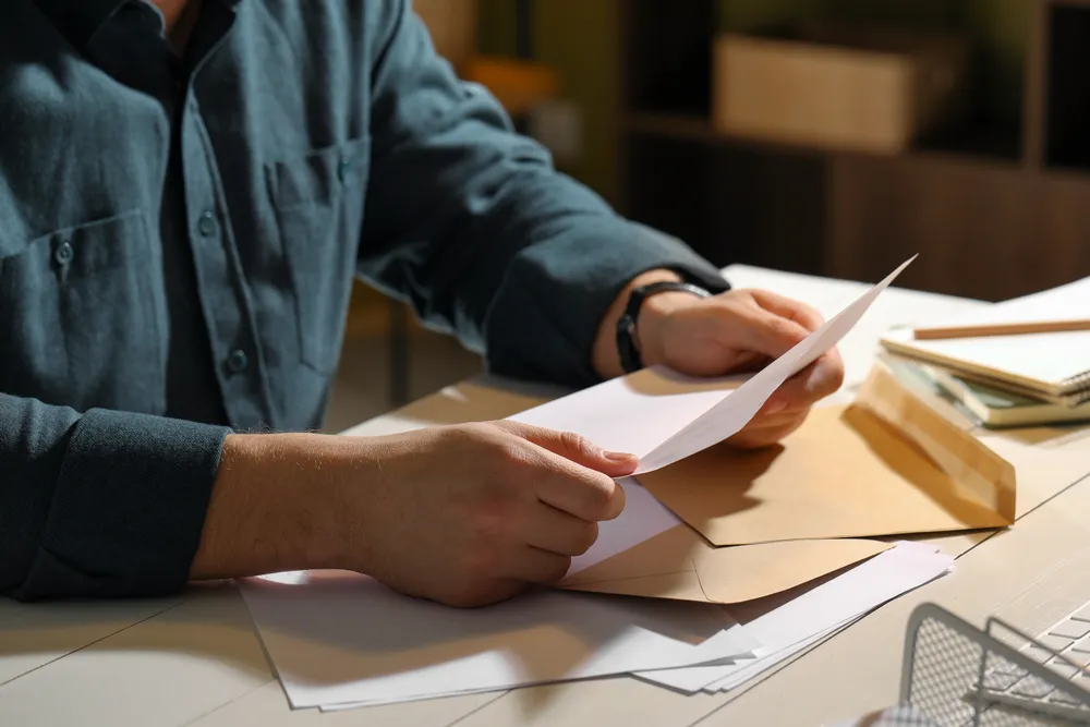 Person at a desk reading a written letter among envelopes, like a prepared written disclosure