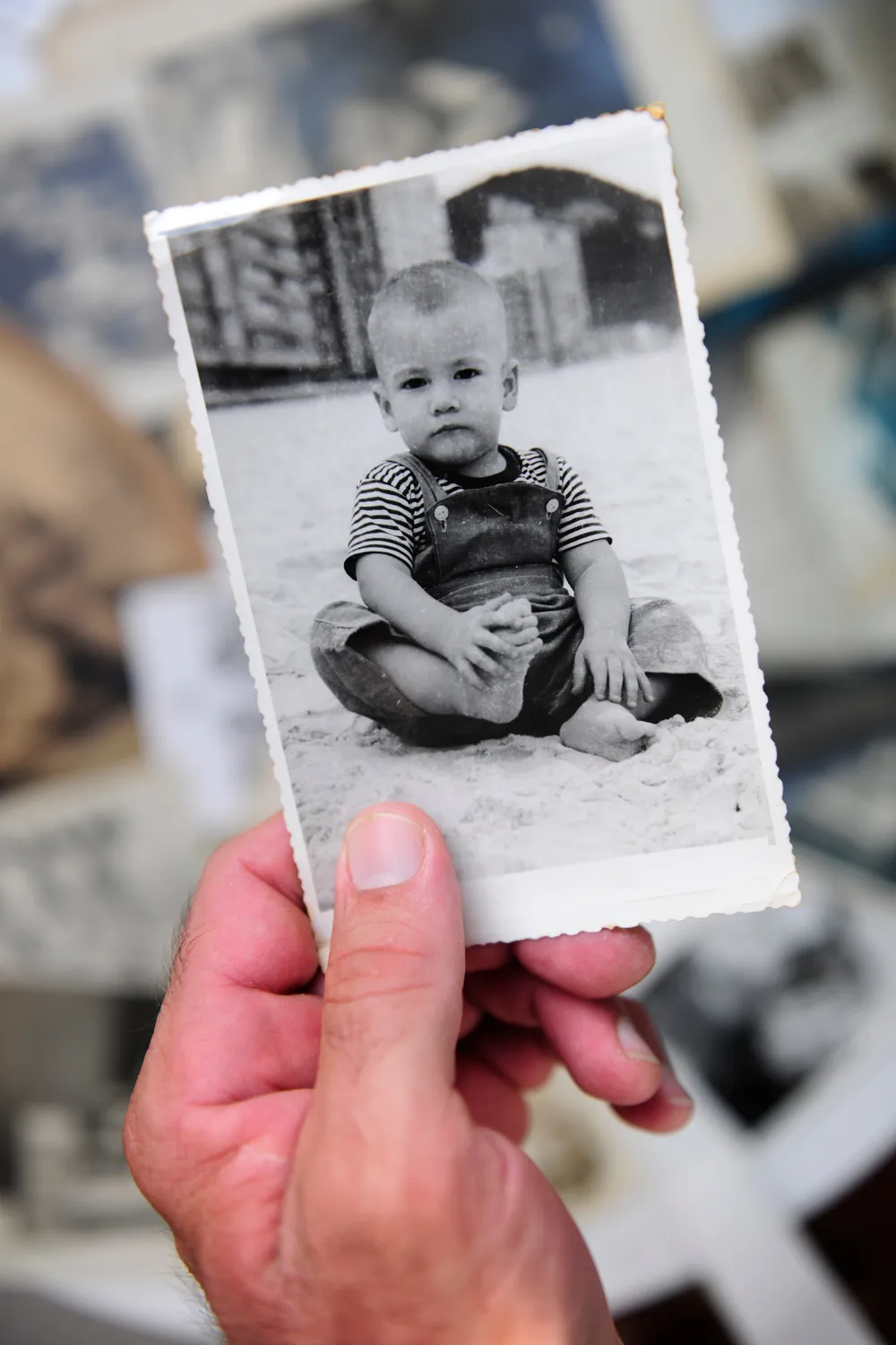 Adult hand holding an old black and white photo of a toddler on a beach, where habitual lying often begins as a childhood survival strategy