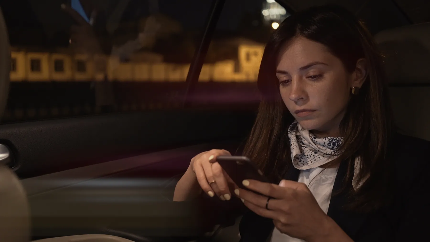 Woman sitting alone in a parked car at night looking down at her phone, weighing how to stop lying in a relationship before she walks inside