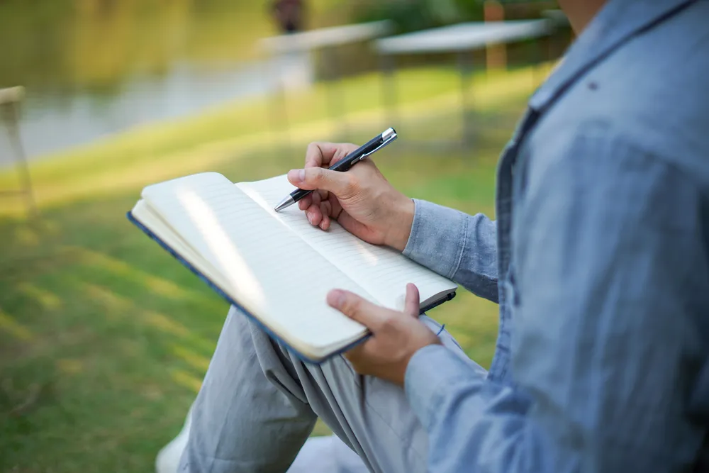 Hands writing in a notebook outdoors, writing out what to say to a partner before a hard conversation