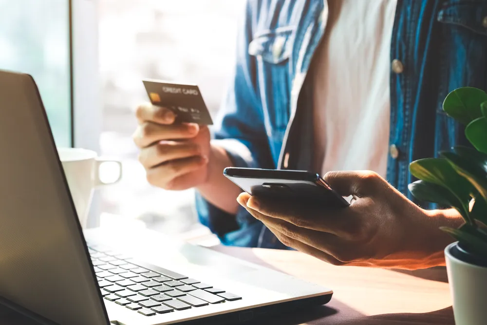 Person holding a credit card and a smartphone at a laptop, the paper trail left by paid interactive adult content