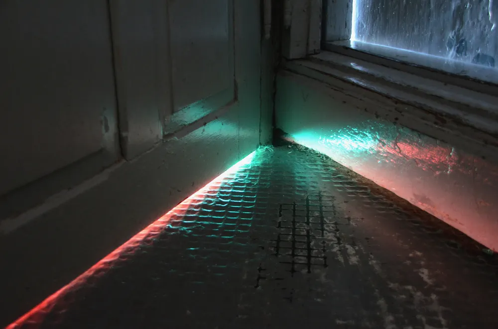 Colored light spilling from under a closed door onto a dark floor, a hint of what happens behind it